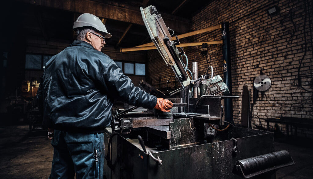 Experienced worker is working at metal factory using special machine tool.