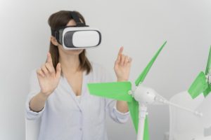 Il settore delle energie rinnovabili diventa importante anche rispetto all'incremento delle intelligenze artificiali, che si basano su sistemi fortemente energivori. Nella foto, una donna con visore per realtà alternativa e il modellino di un impianto eolico vicino.